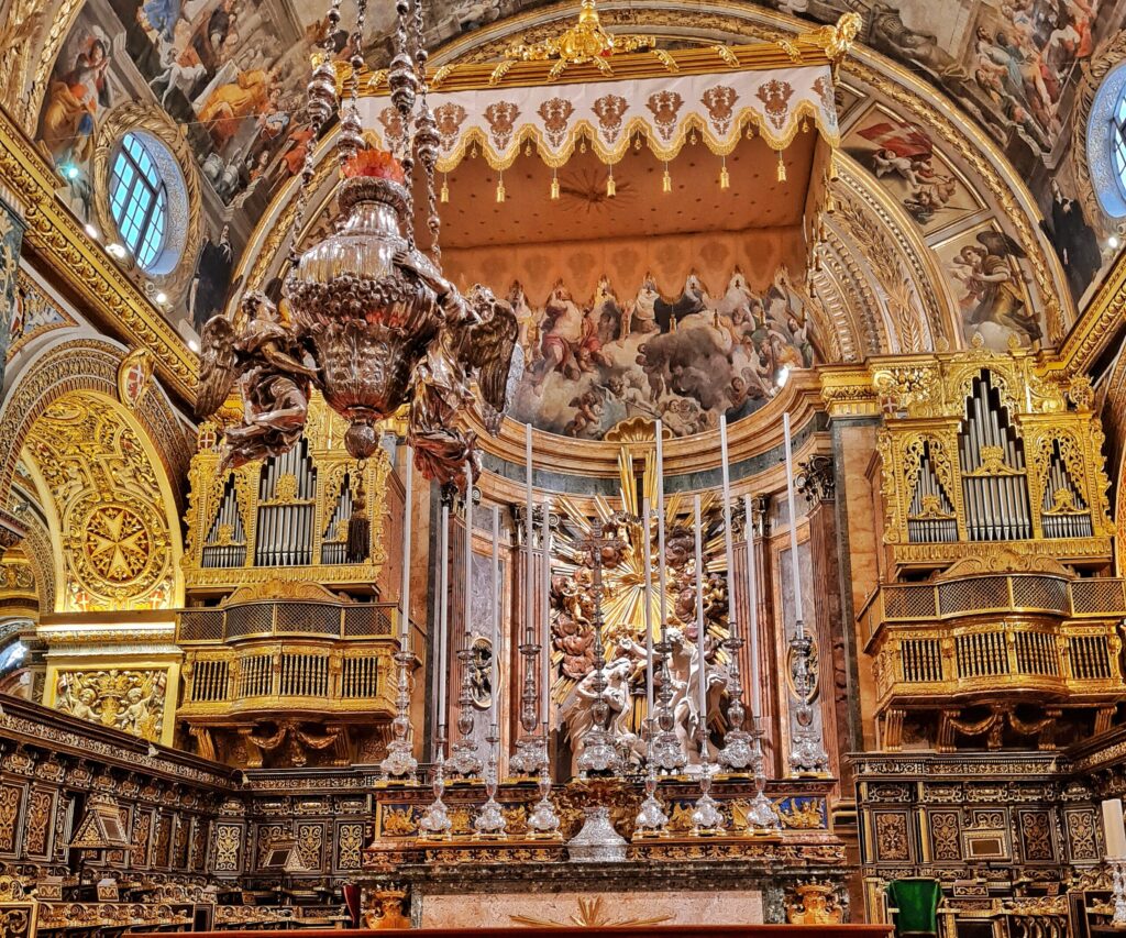 Blick auf den Altar mit dem Baldachin darüber und dem daneben hängenden Gefäß von vorne fotografiert. Links und rechts jeweils eine goldene Orgel.