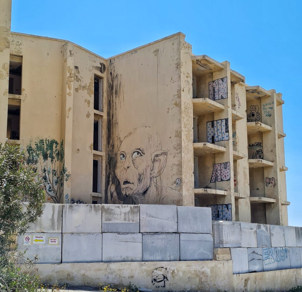 Ein Teil eines vierstöckigen Hrbäudes mit leeren Fensteröffnungen. Es ist teilweise mit Graffiti bemalt, darunter eine große Zeichnung von Gollum.