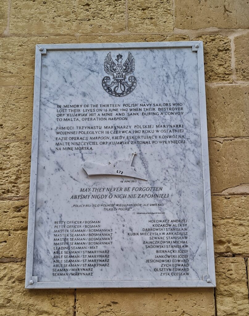 Eine an einer Mauer angebrachte große Tafel aus weißem Stein mit grauen Marmorierungen. Der Text darauf ist auf polnisch und englisch. Er erinnert an 13 polnische Marinesoldaten, die getötet wurden, als ihr Zerstörer am 16. Juni 1942 auf eine Mine lief. Darunter ist ein stilisiertes Kriegsschiff und die Worte "May they never be forgotten" (auch auf polnisch). Ganz unten die Namen und Dienstgrade der 13 Polen.