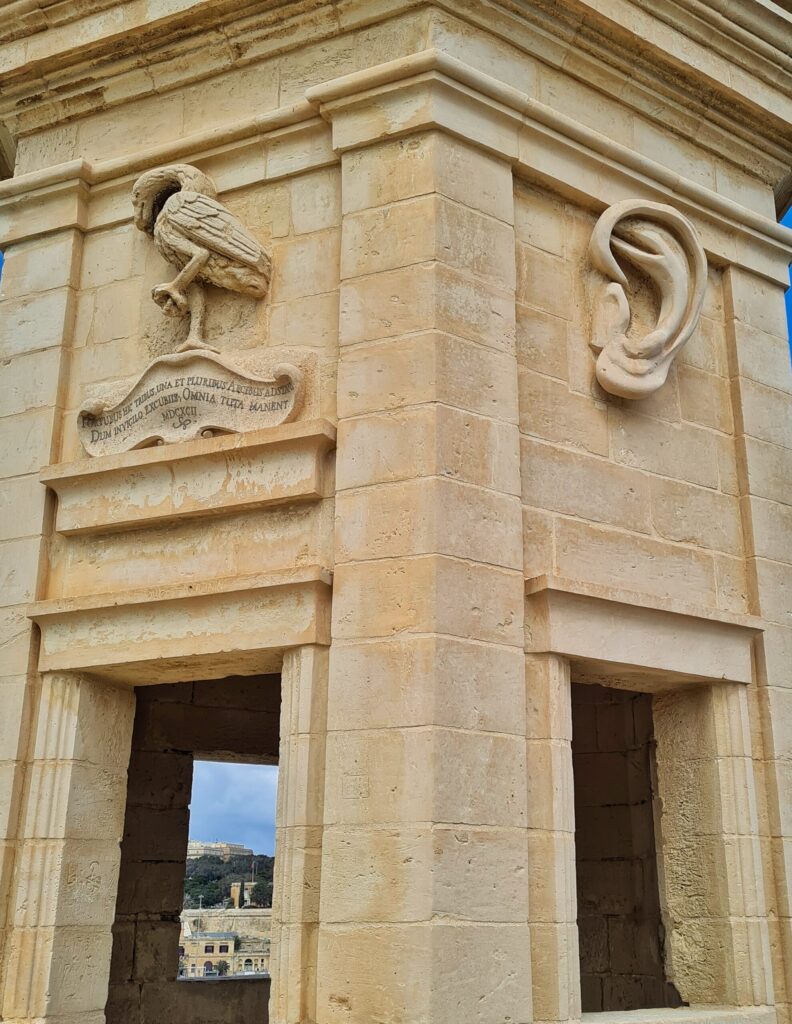 Der Turm aus der Nähe fotografiert. Unten sieht man durch eine Öffnung auf Bäume und Gebäude. Darüber die Darstellung eines laufenden Vogels, und an der anderen Turmwand ein Ohr.