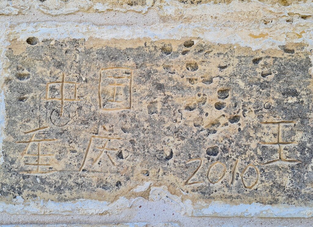 Ein ziemlich abgeblätterter Stein, in den Schriftzeichen (chinesisch oder ähnliches) und 2010 eingeritzt sind.