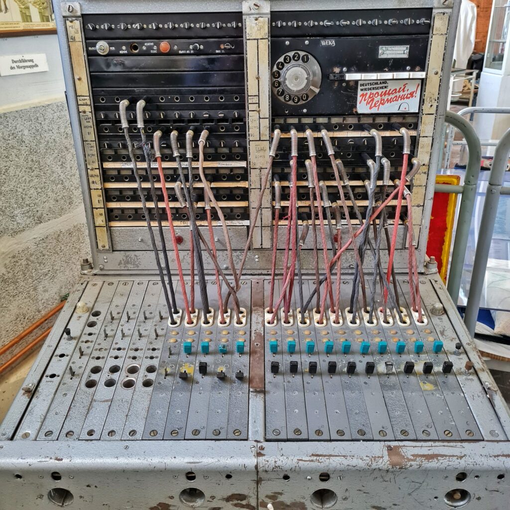 Eine alte Fernmeldeanlage. Kabel sind von der waagerechten zur senkrechten Schalterfläche gesteckt. Oben rechts ist eine Wählscheibe.