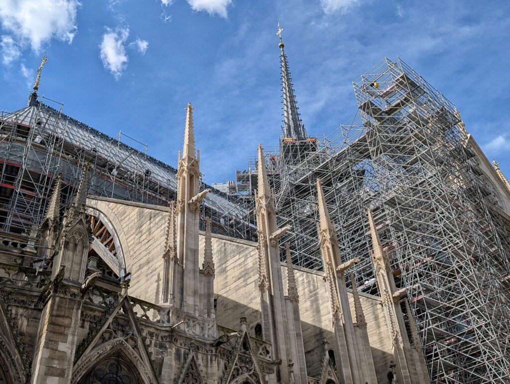 Blick auf die Kathedrale Notre-Dame de Paris, die derzeit restauriert wird, mit Gerüst und blauen Himmel im Hintergrund.
